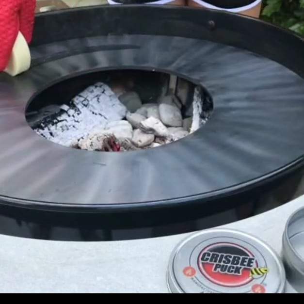 Crisbee Puck seasoning puck placed in grill firebox above gray ash