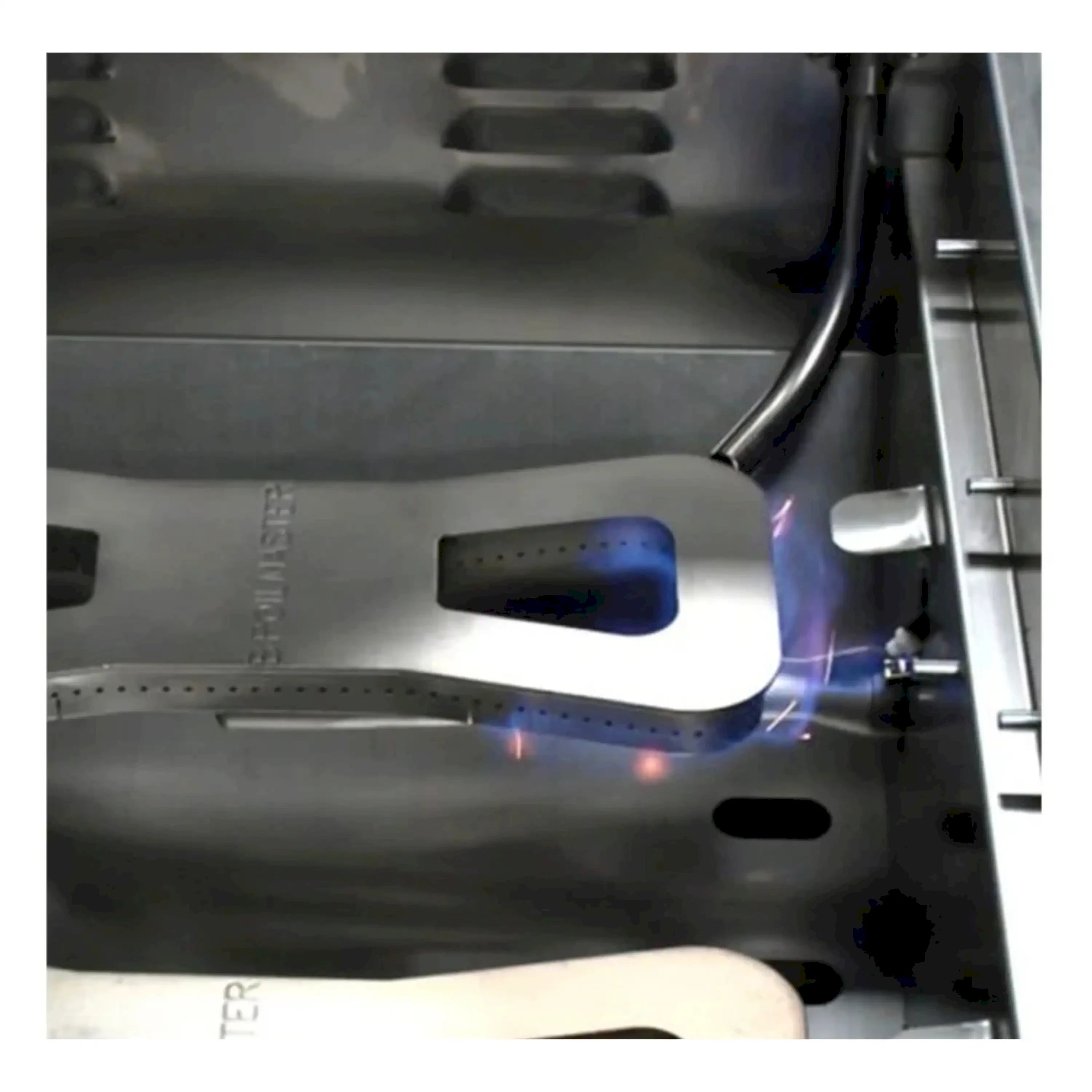 Stainless propane grill burner area with blue flame on cooking surface