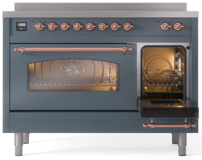 Blue-grey induction range with one oven door open, copper handle, and lit oven cavity.