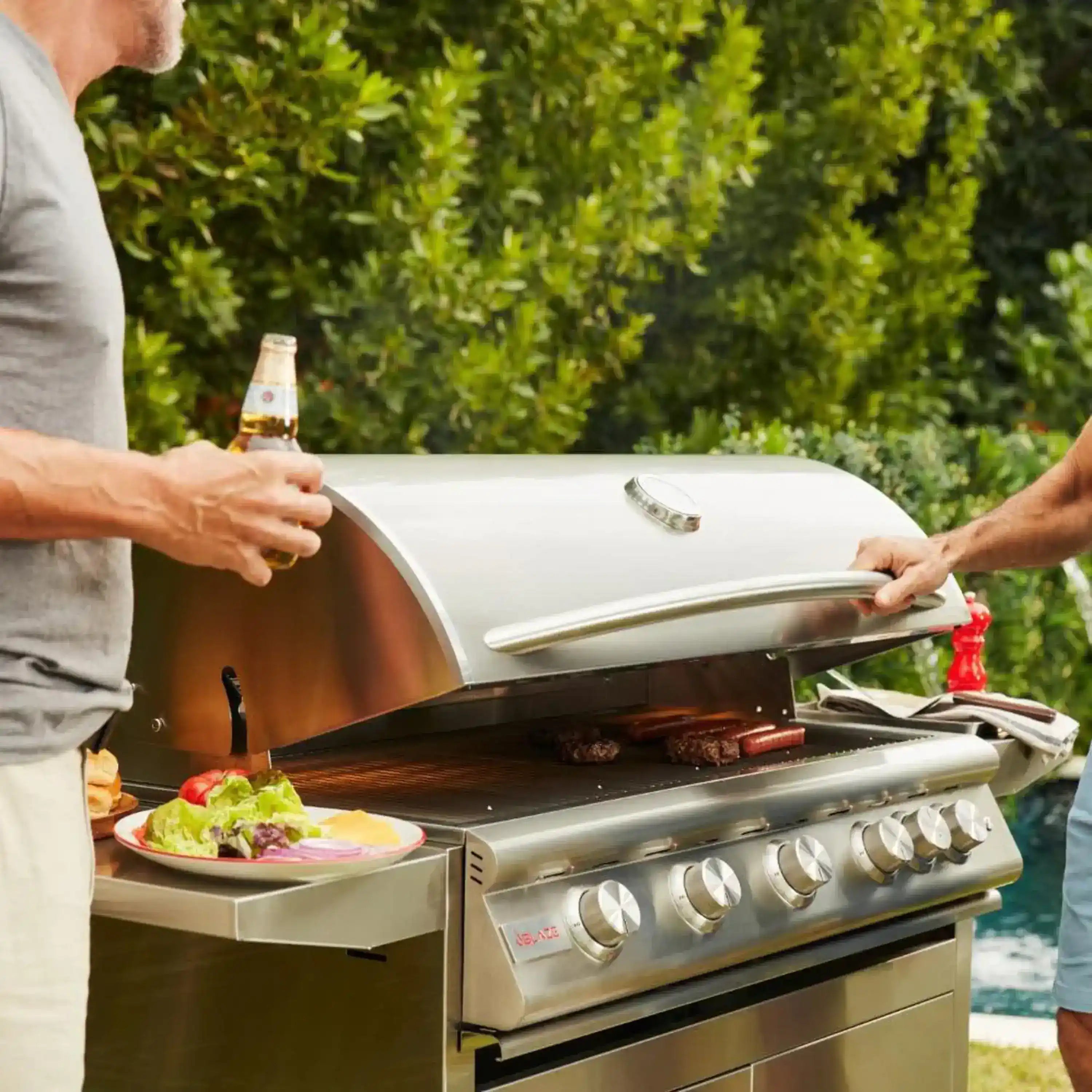 Stainless steel natural gas grill with lid open, burners on, and cooking grates visible