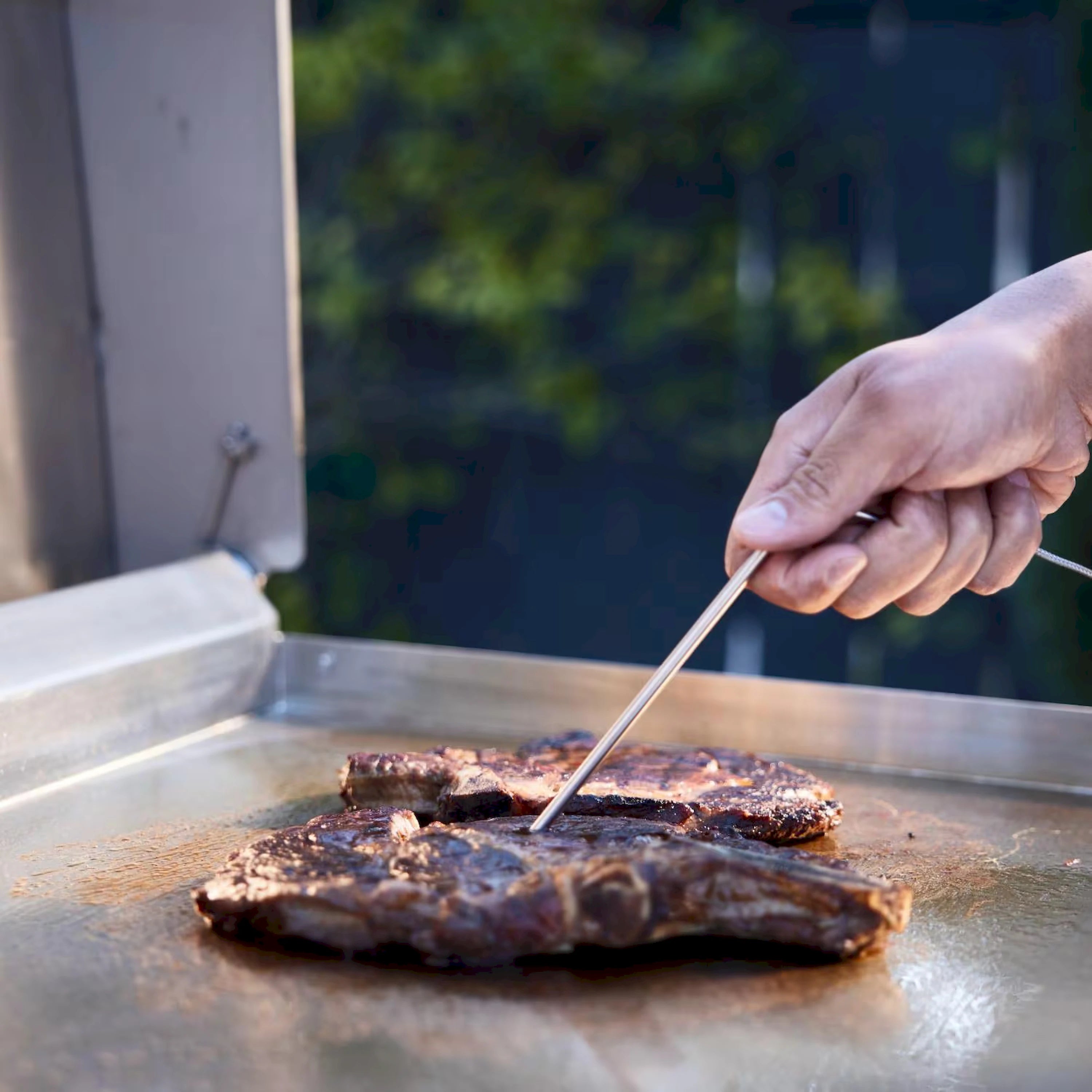 Stainless steel gas griddle with lid open, food searing on flat cooktop