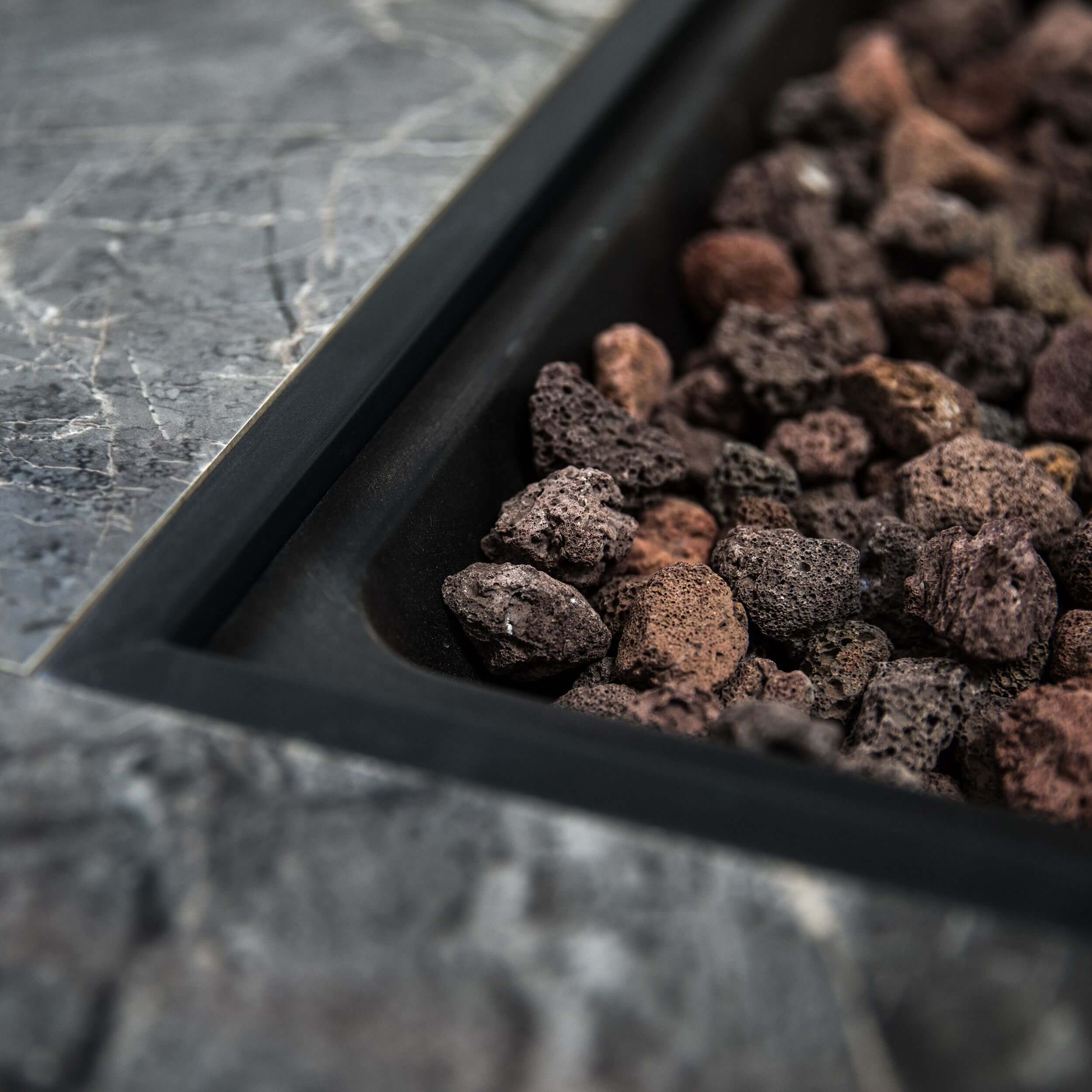 Close-up of lava rocks inside the firepit bowl with gray stone surround