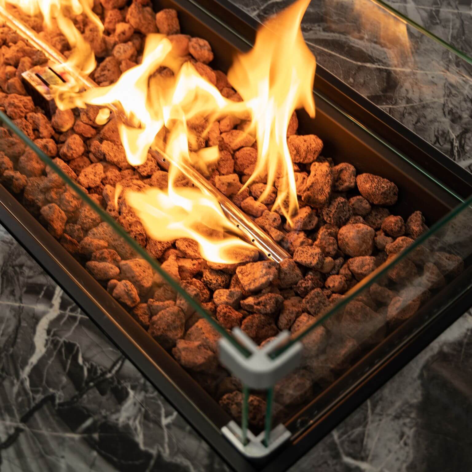 Propane fire pit burner with flames over lava rocks in glass tray
