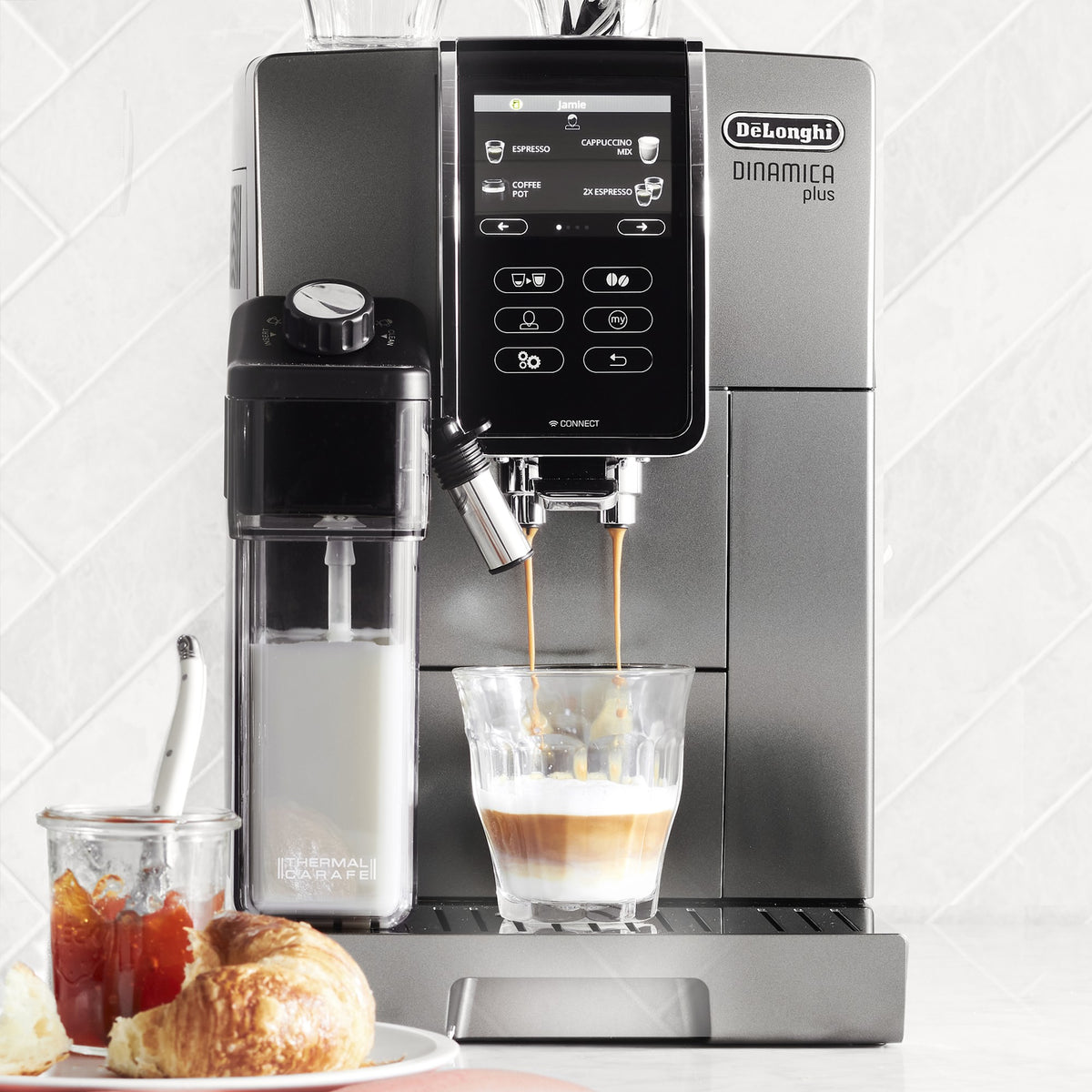 Titanium super-automatic espresso machine dispensing into a clear cup with coffee and milk
