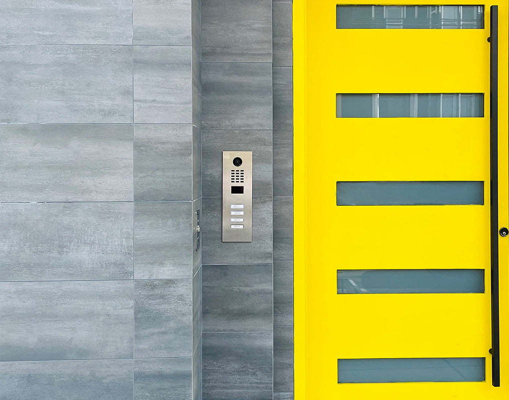 Stainless DoorBird IP video door station on wall with camera, keypad, and 4 call buttons
