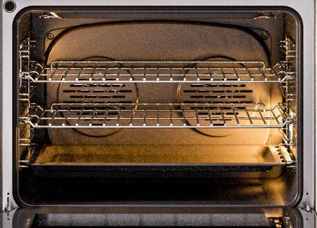 Open oven cavity of white induction range with wire racks and warm interior light
