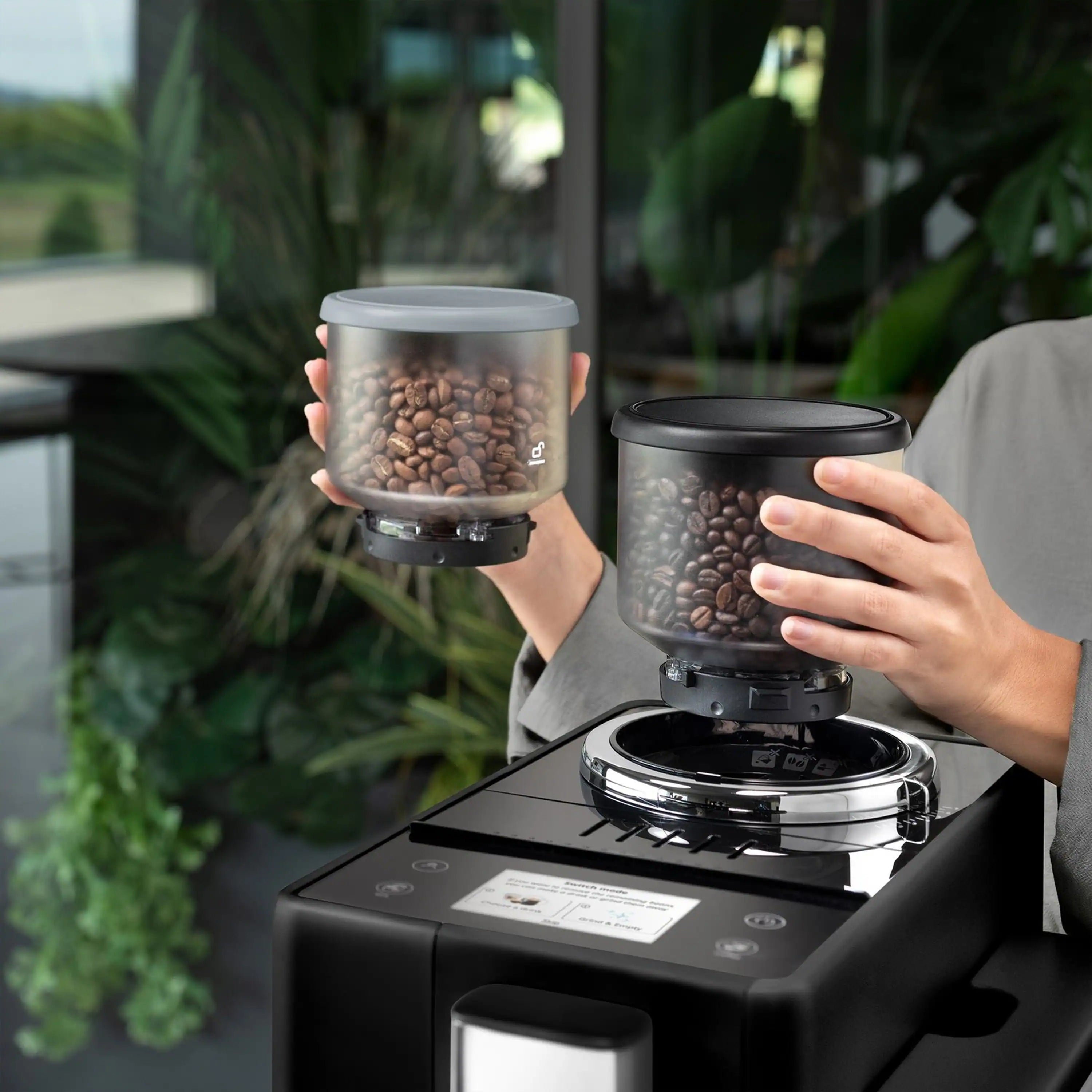 Black fully automatic espresso machine with open bean hopper, hands holding coffee beans