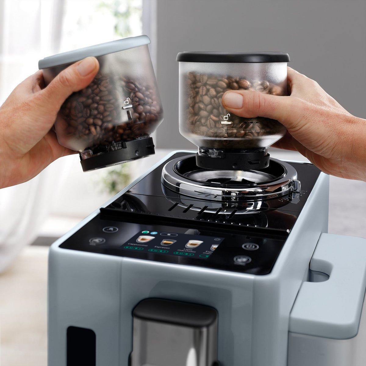 De'Longhi Rivelia espresso machine with hands placing coffee bean containers on top