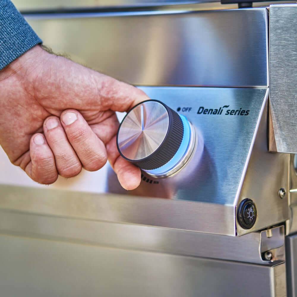 Stainless steel grill control knob turned by hand, Denali Series label visible