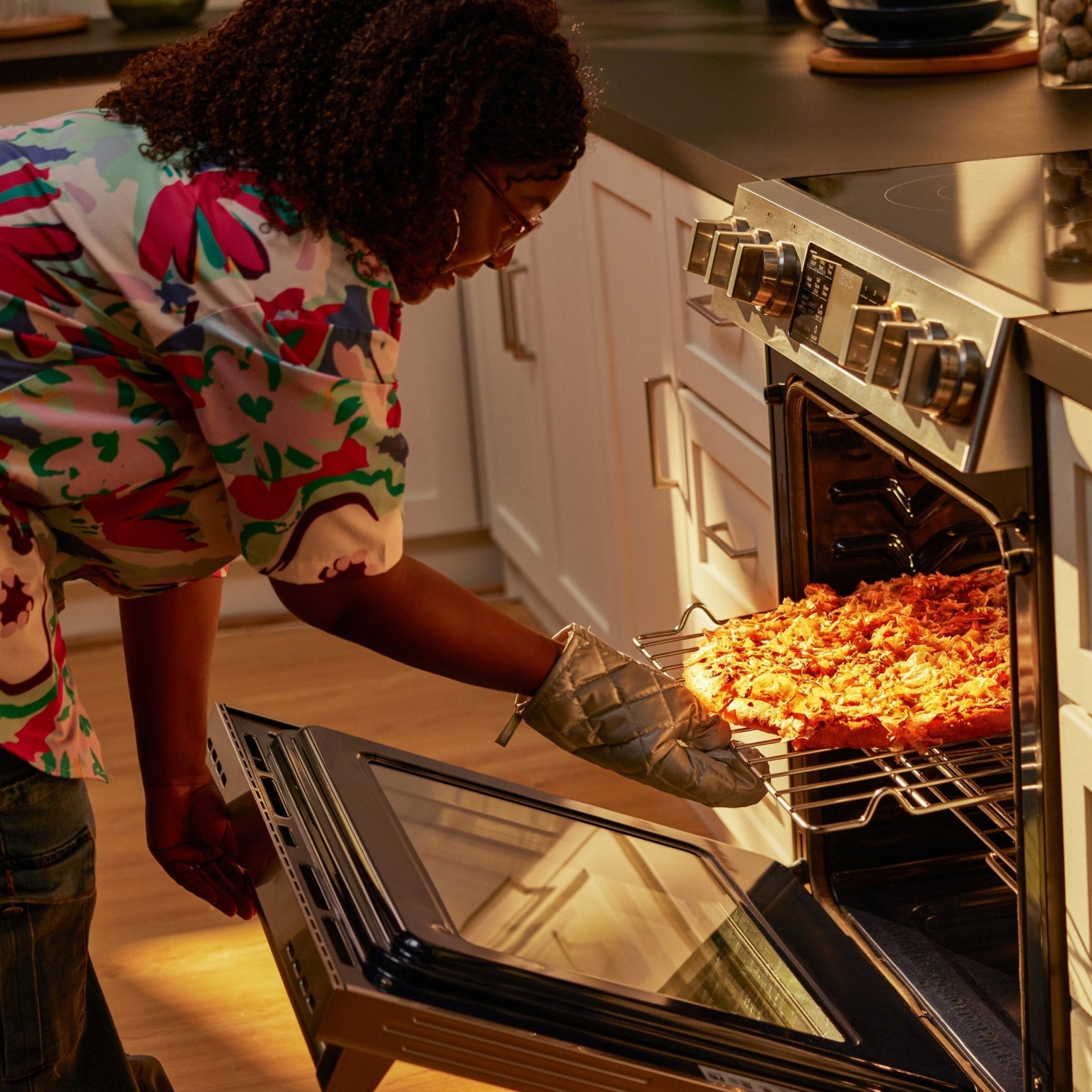 Stainless slide-in electric range with oven door open and food on a baking tray