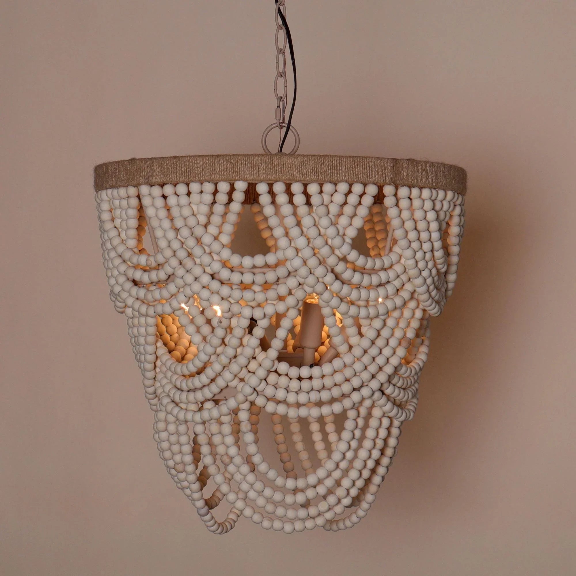 White beaded chandelier with beige fabric rim and warm glowing bulb cutouts