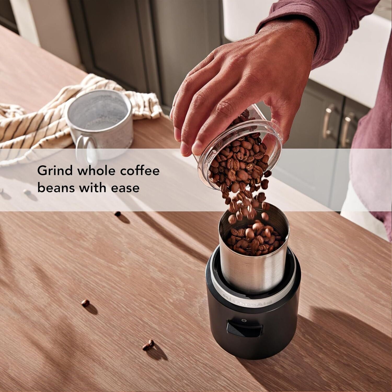 Whole coffee beans being poured into a black cordless grinder with stainless chamber and clear lid