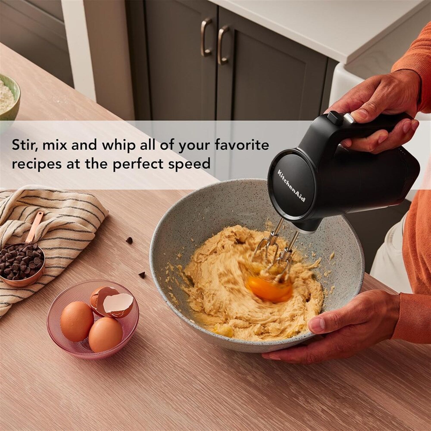 KitchenAid cordless hand mixer stirring batter in a bowl, held in black matte