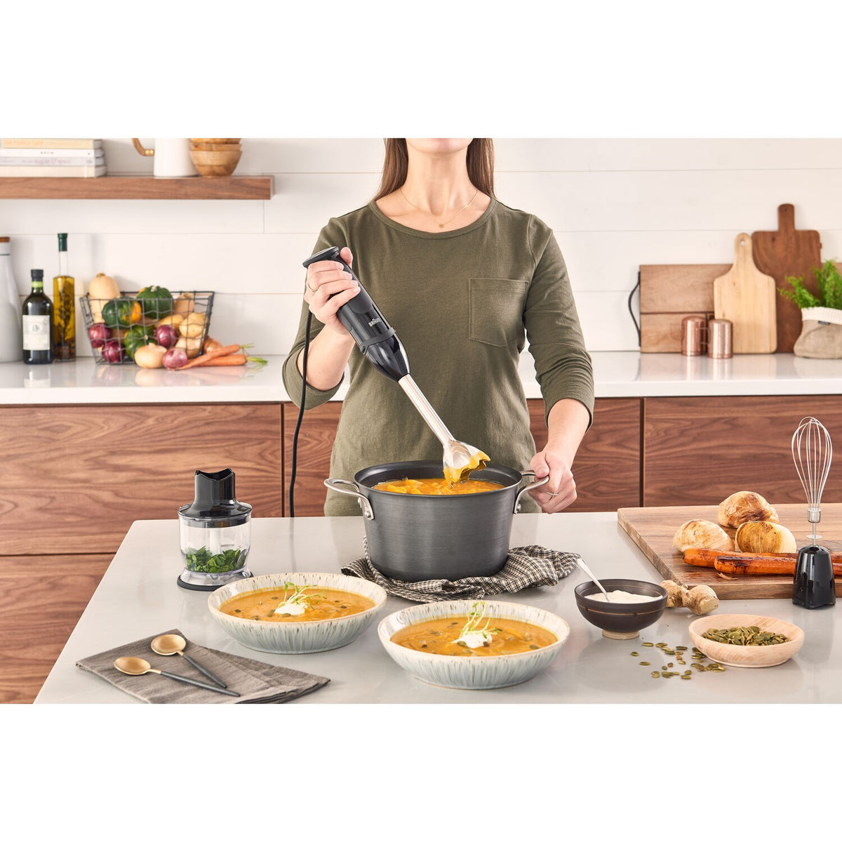 Black hand blender mixing food in a pot with a metal whisk attachment.