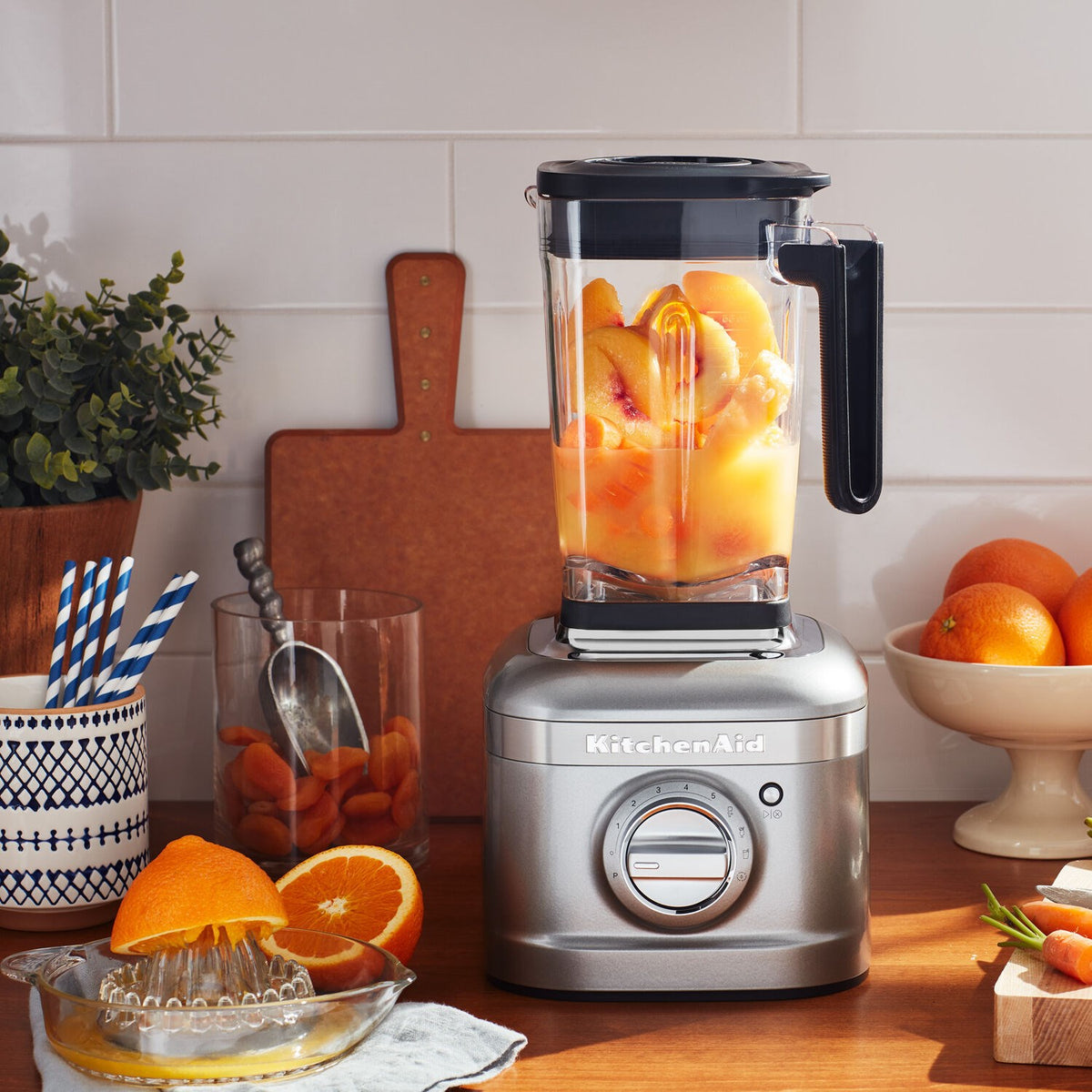 KitchenAid blender with clear jar filled with orange ingredients, contour silver base