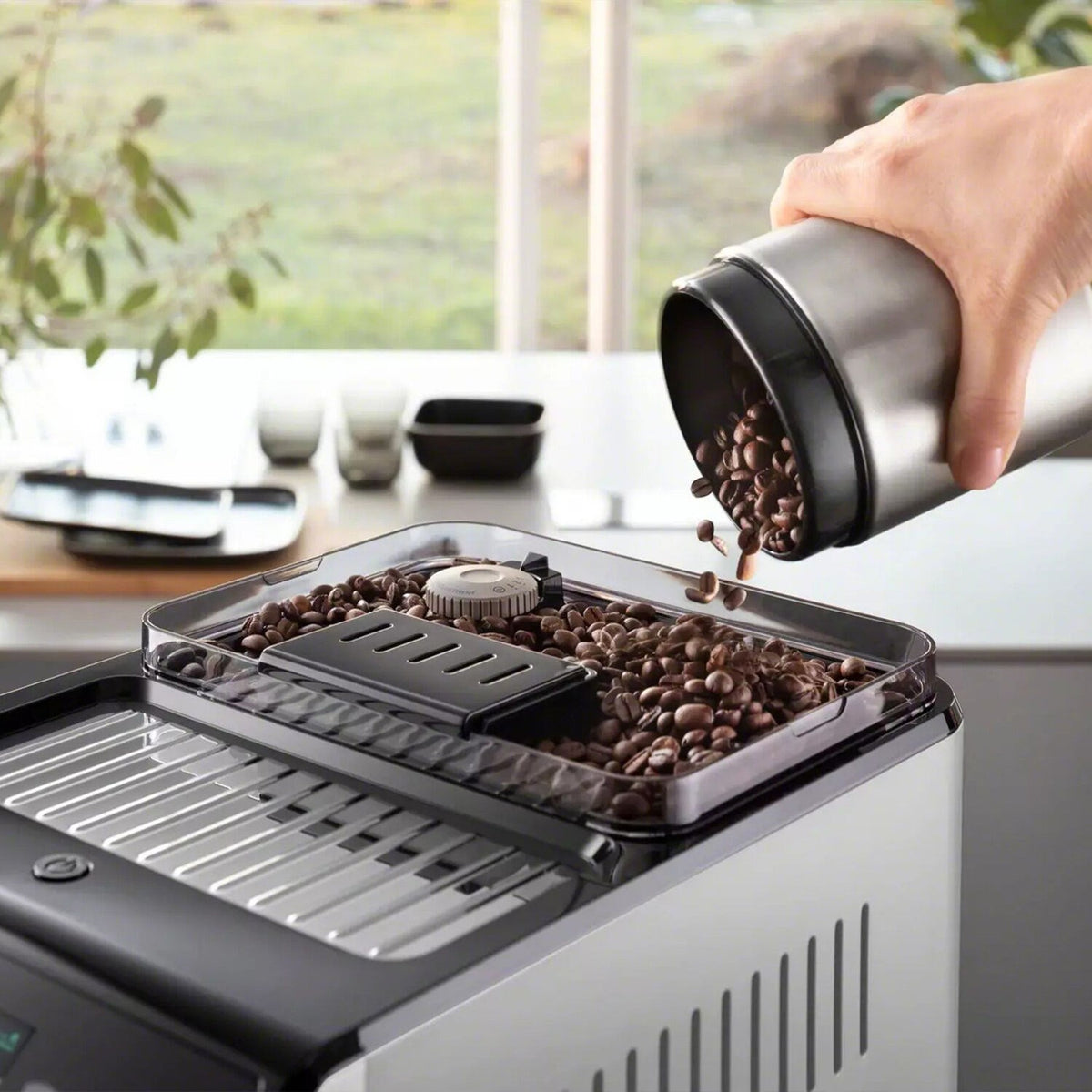 Fully automatic espresso machine: hand pouring coffee beans into grinder hopper