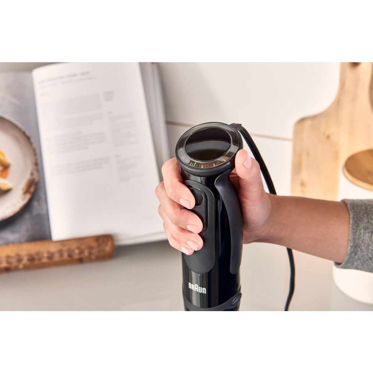 Black Braun hand blender held in hand, showing control buttons and cord.
