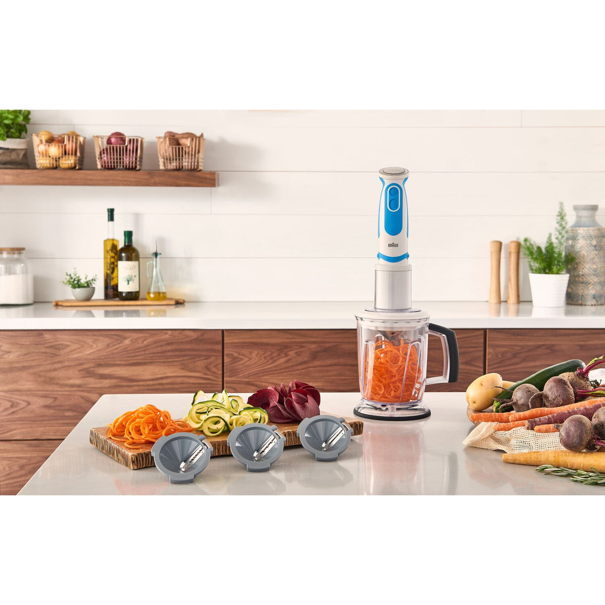 Hand blender and multiple spiralizer heads with sliced vegetables on countertop