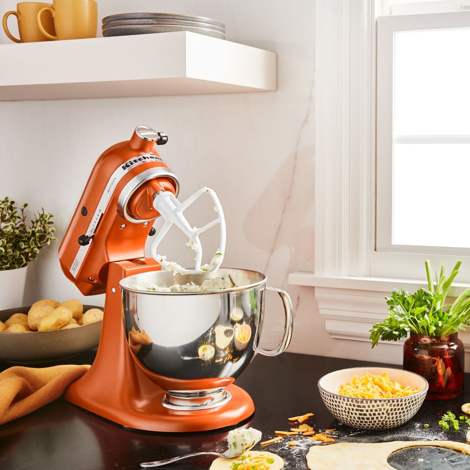 KitchenAid Artisan tilt-head stand mixer in scorched orange with stainless mixing bowl and whisk