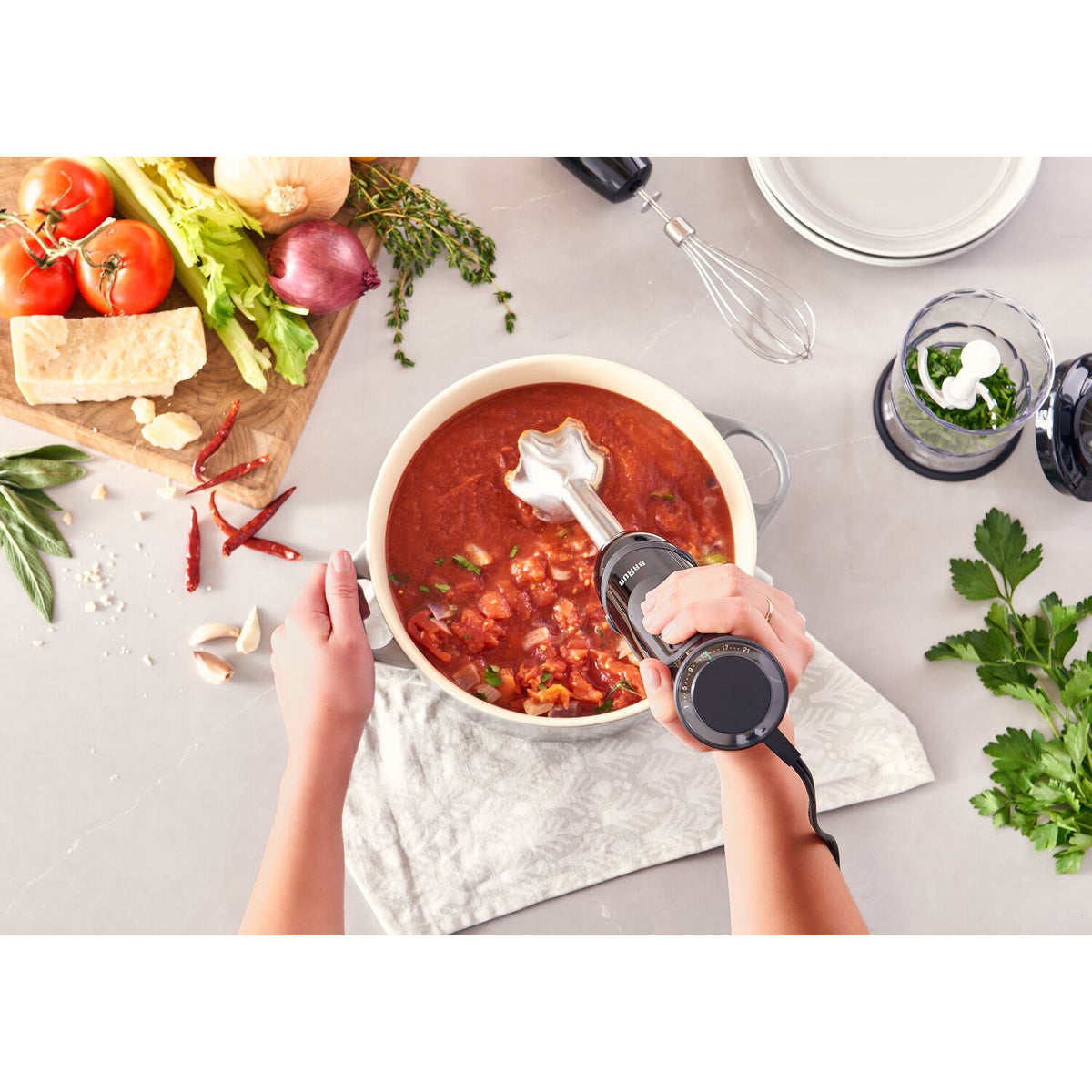Hand blender blending soup in a bowl with the whisk attachment over vegetables.