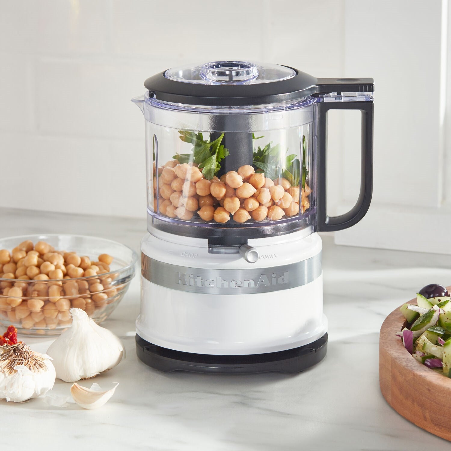 White countertop food chopper with transparent bowl filled with ingredients and black handle