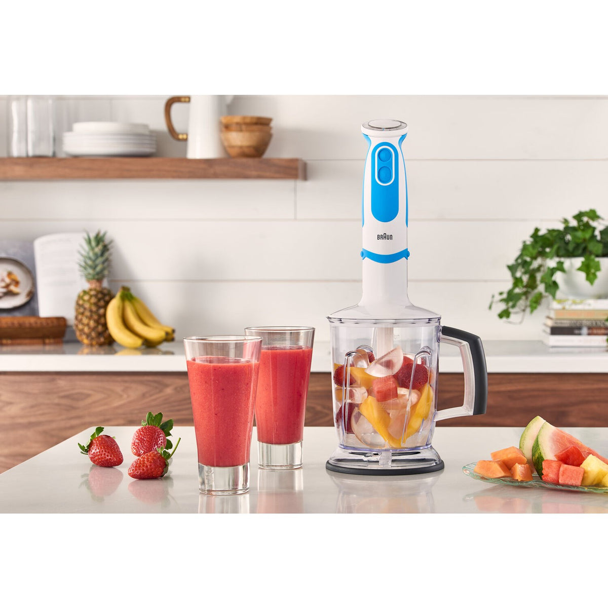 Hand blender on countertop with blender cup and mixed fruit smoothies