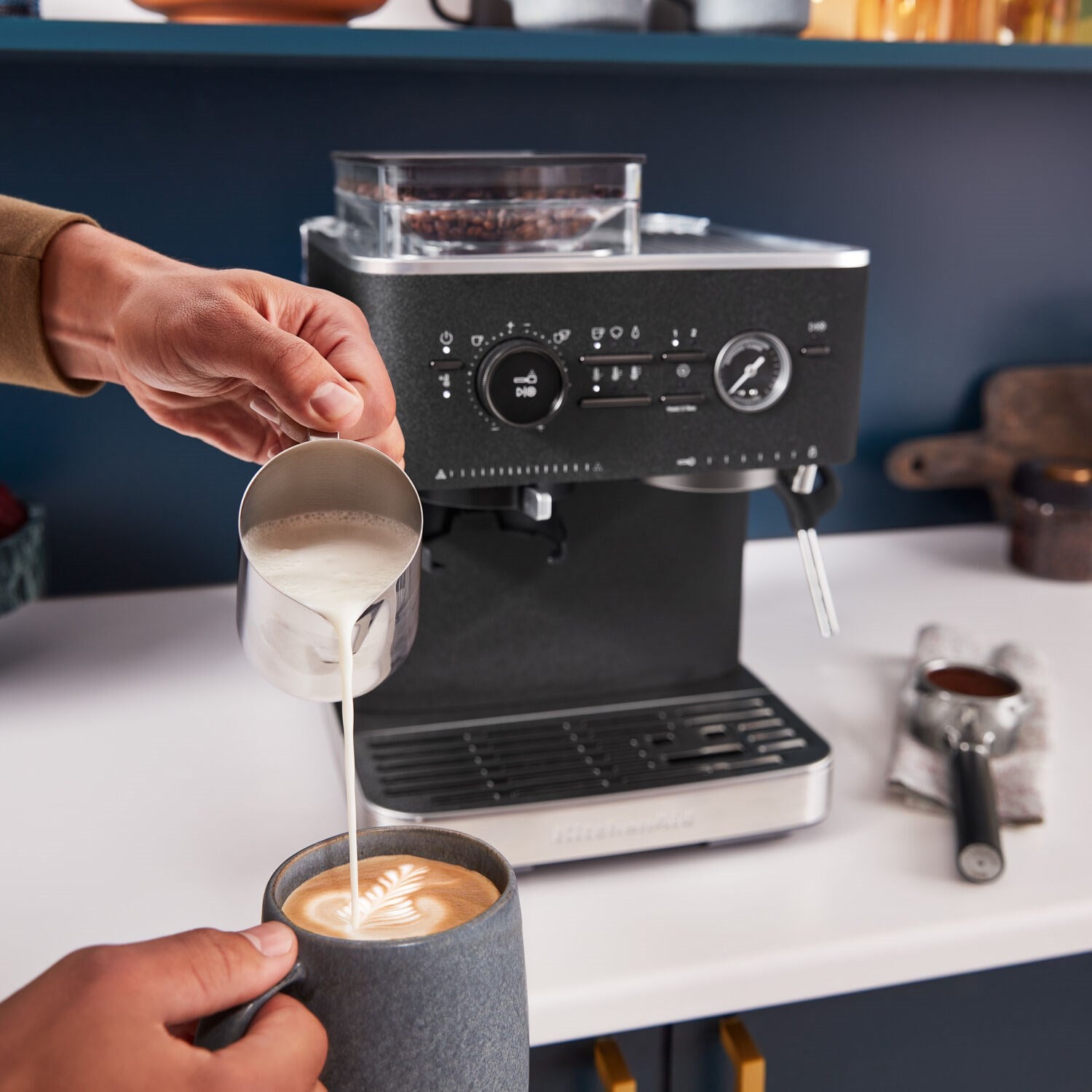 Black espresso machine with grinder hopper; hand pours espresso into a cup