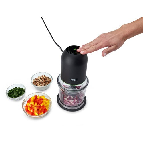 Hand pressing black mini food chopper lid; clear bowl with chopped vegetables inside
