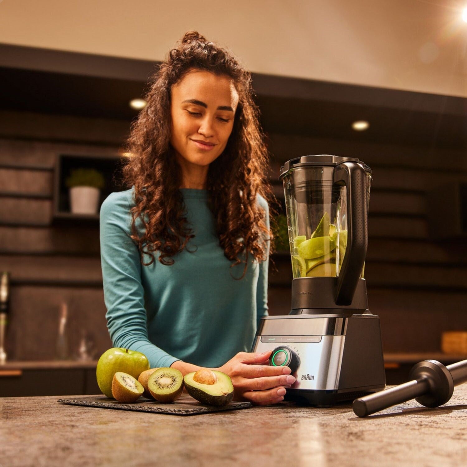 Person preparing blended fruit in a black blender on a kitchen counter with ingredients.