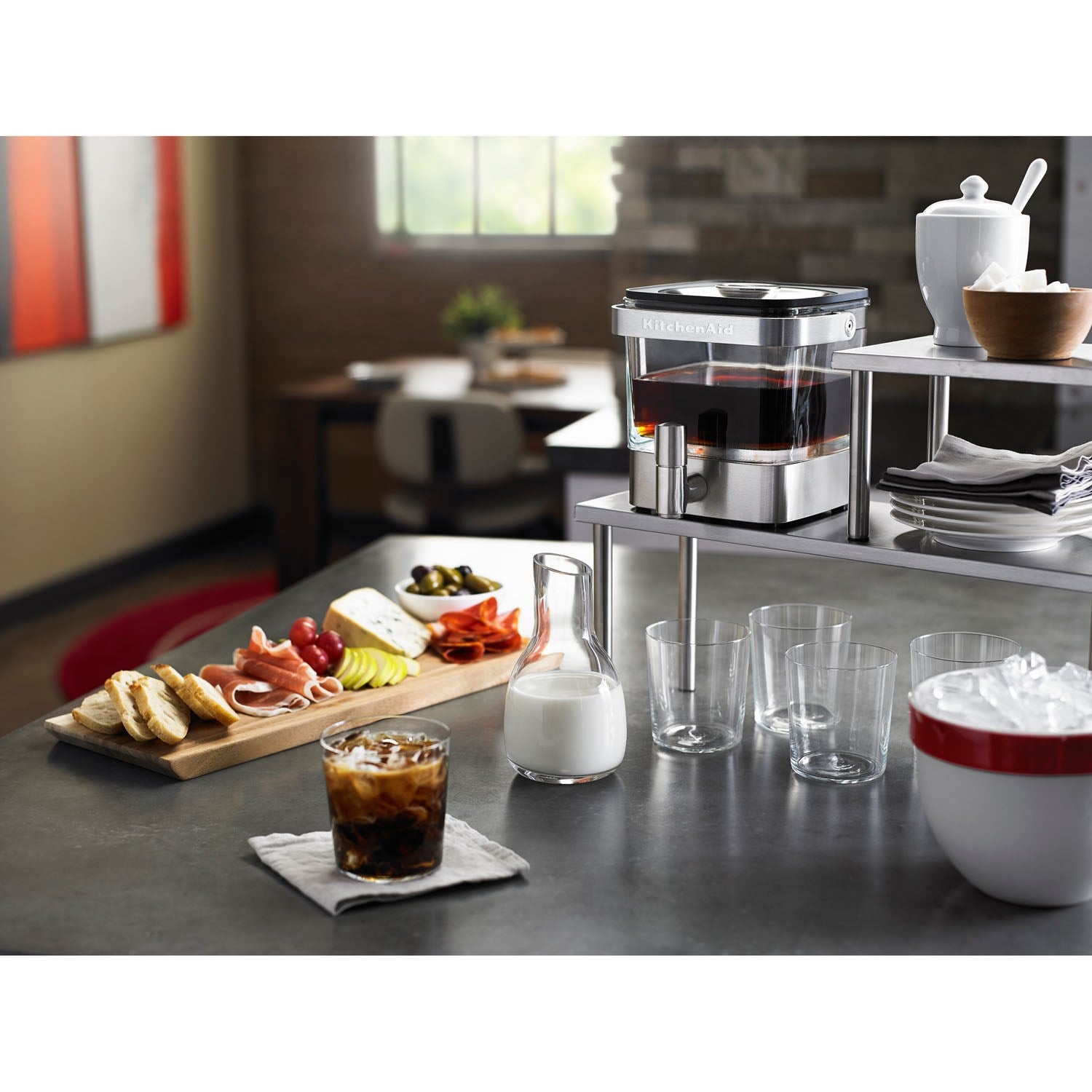 Brushed stainless cold brew coffee maker on countertop with glasses and pitcher nearby