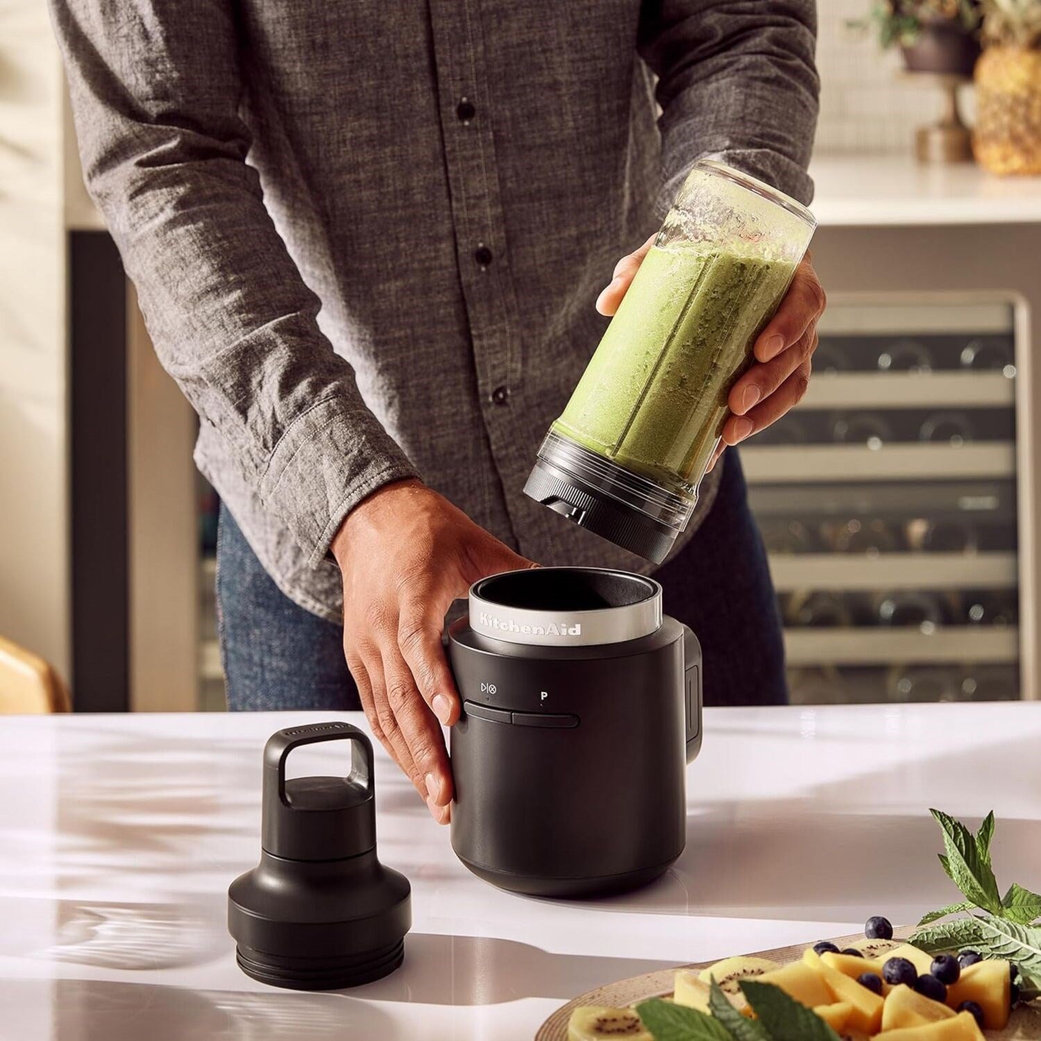 Black personal blender with clear jar and to-go cup, held with a green drink