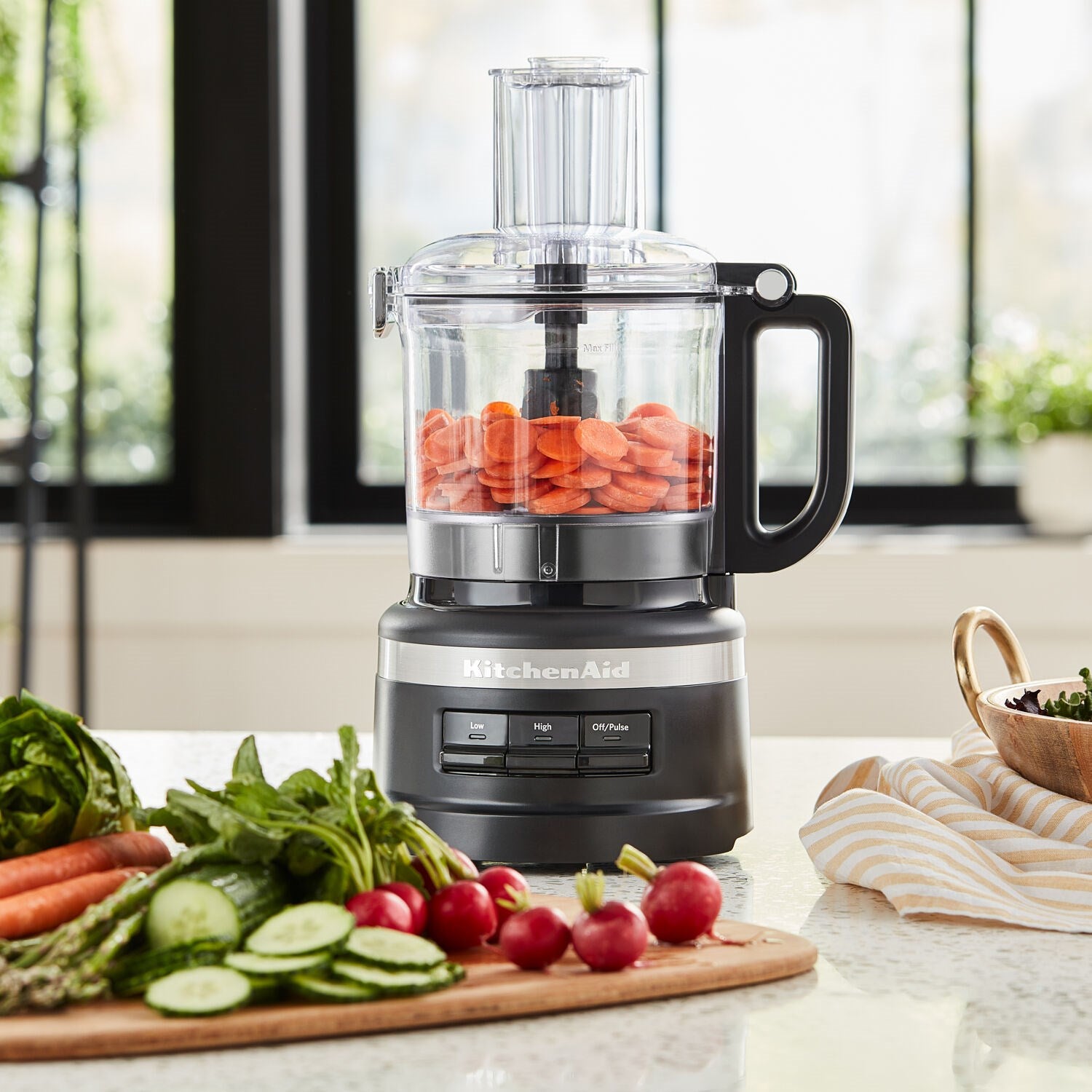 Black matte food processor with clear bowl filled with carrots on countertop