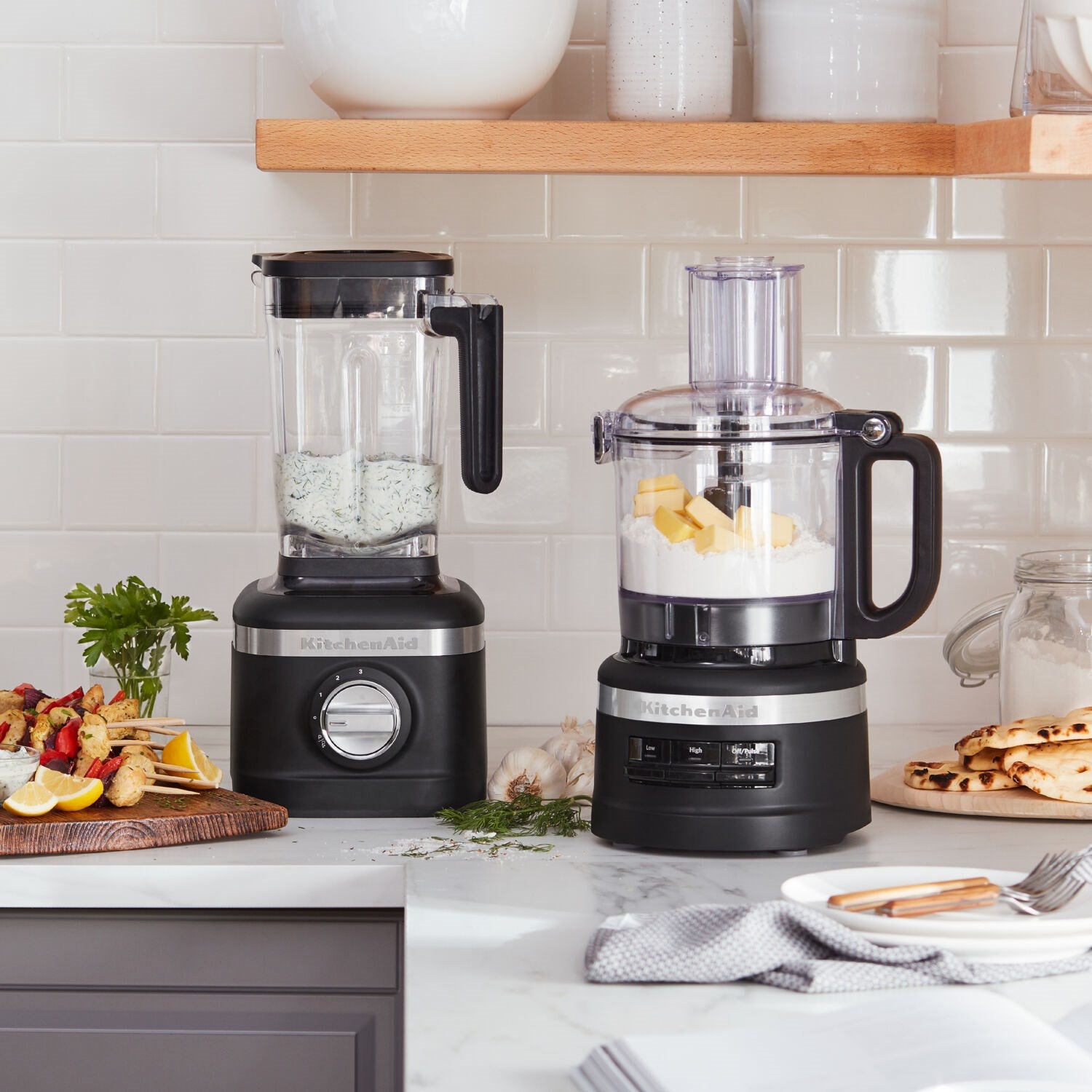 Two black matte food processors with clear bowls on kitchen countertop
