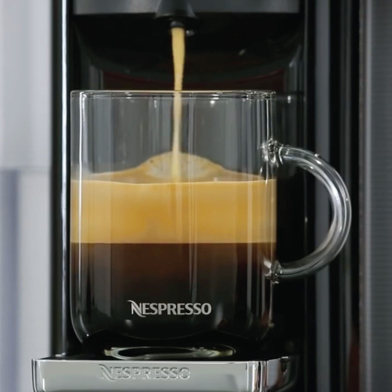 Clear mug under espresso spout with layered crema in the cup