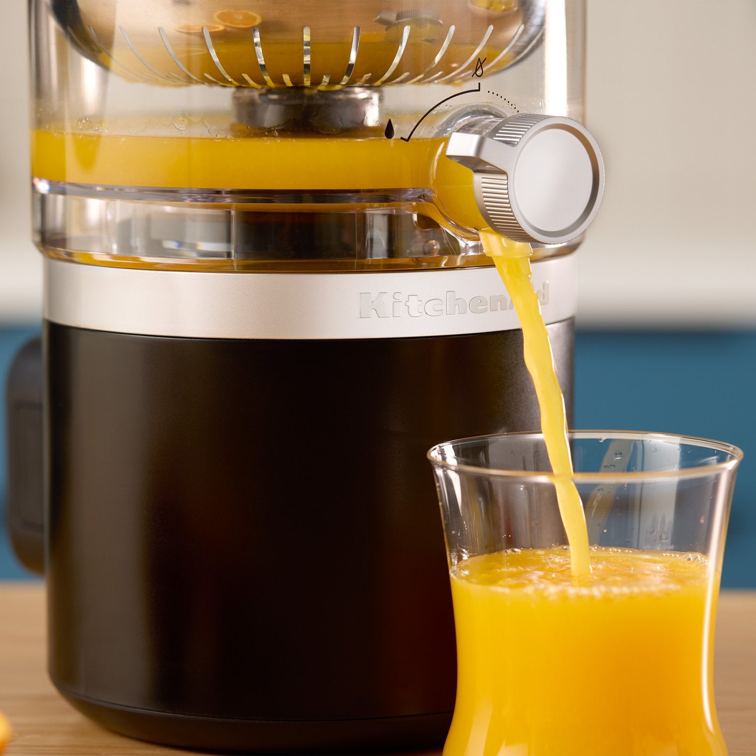 Citrus juicer spout pouring orange juice into a clear glass