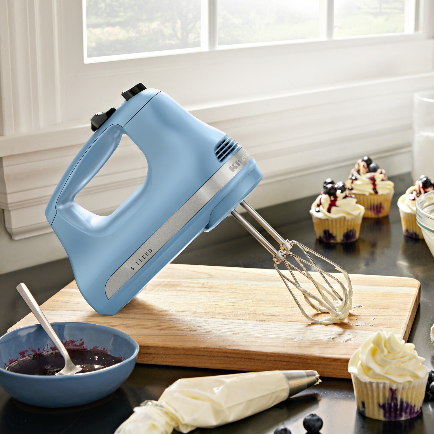 Blue KitchenAid 5-speed hand mixer with two metal beaters on a countertop
