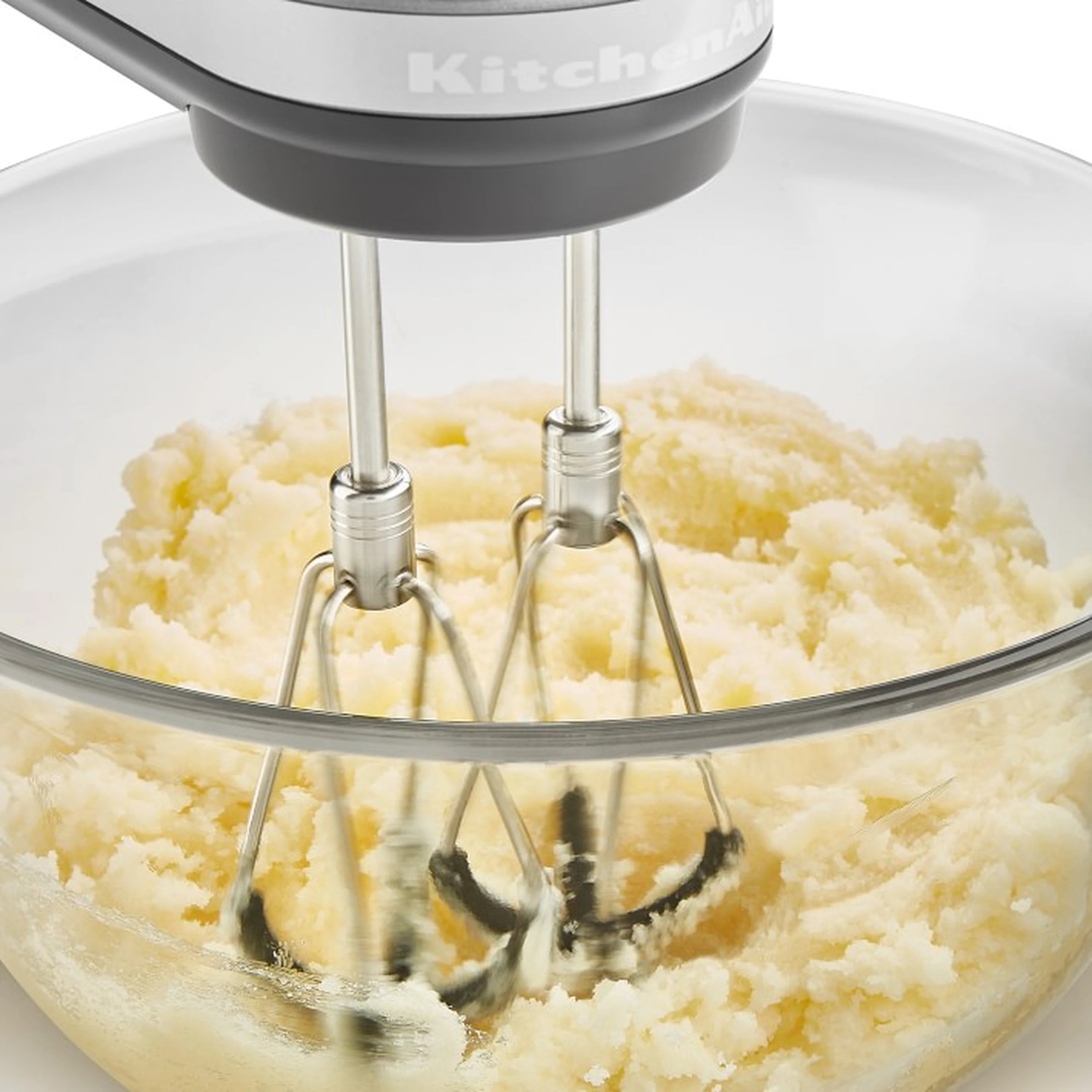 Stainless beaters mixing pale batter in a clear bowl