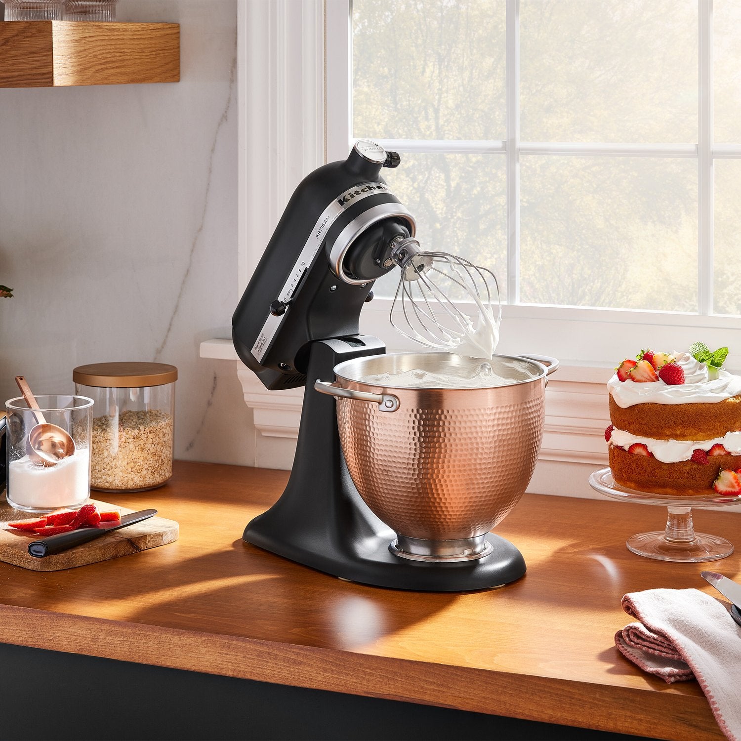Copper hammered mixing bowl mounted on black stand mixer with whisk attachment