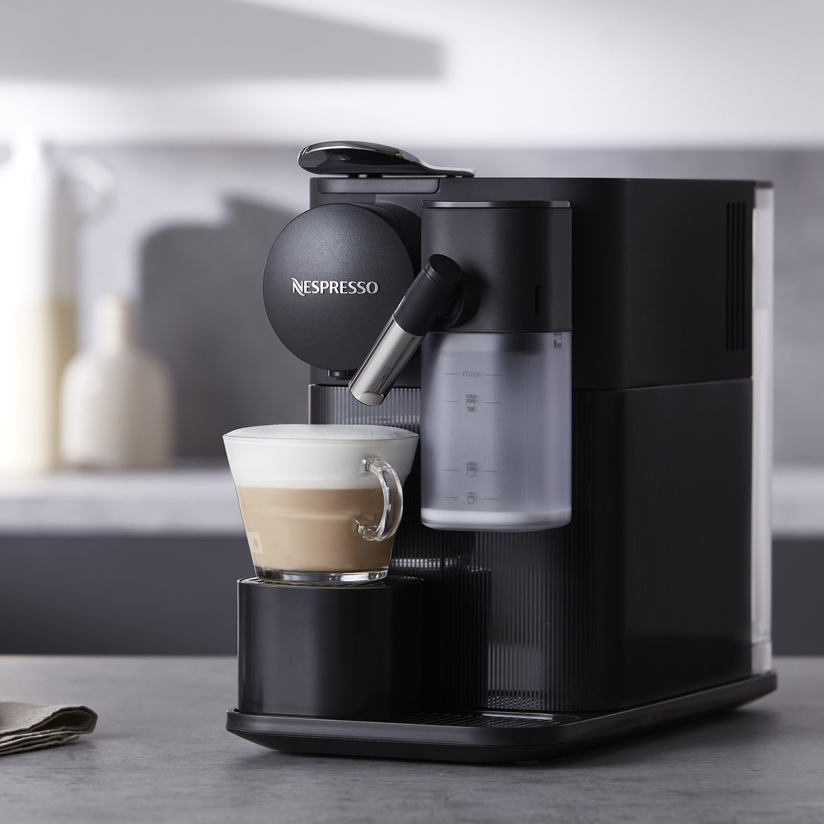 Black Nespresso espresso machine brewing into a glass mug with crema layer