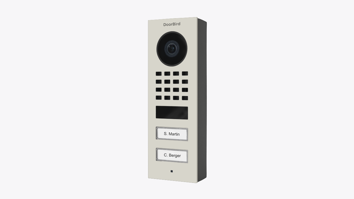 DoorBird surface-mount IP video door station, grey housing with camera lens, speaker grille, and two call buttons