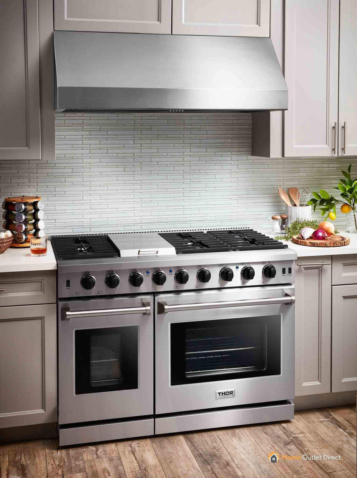 Stainless steel gas range with griddle, burners, and two oven doors under wall hood