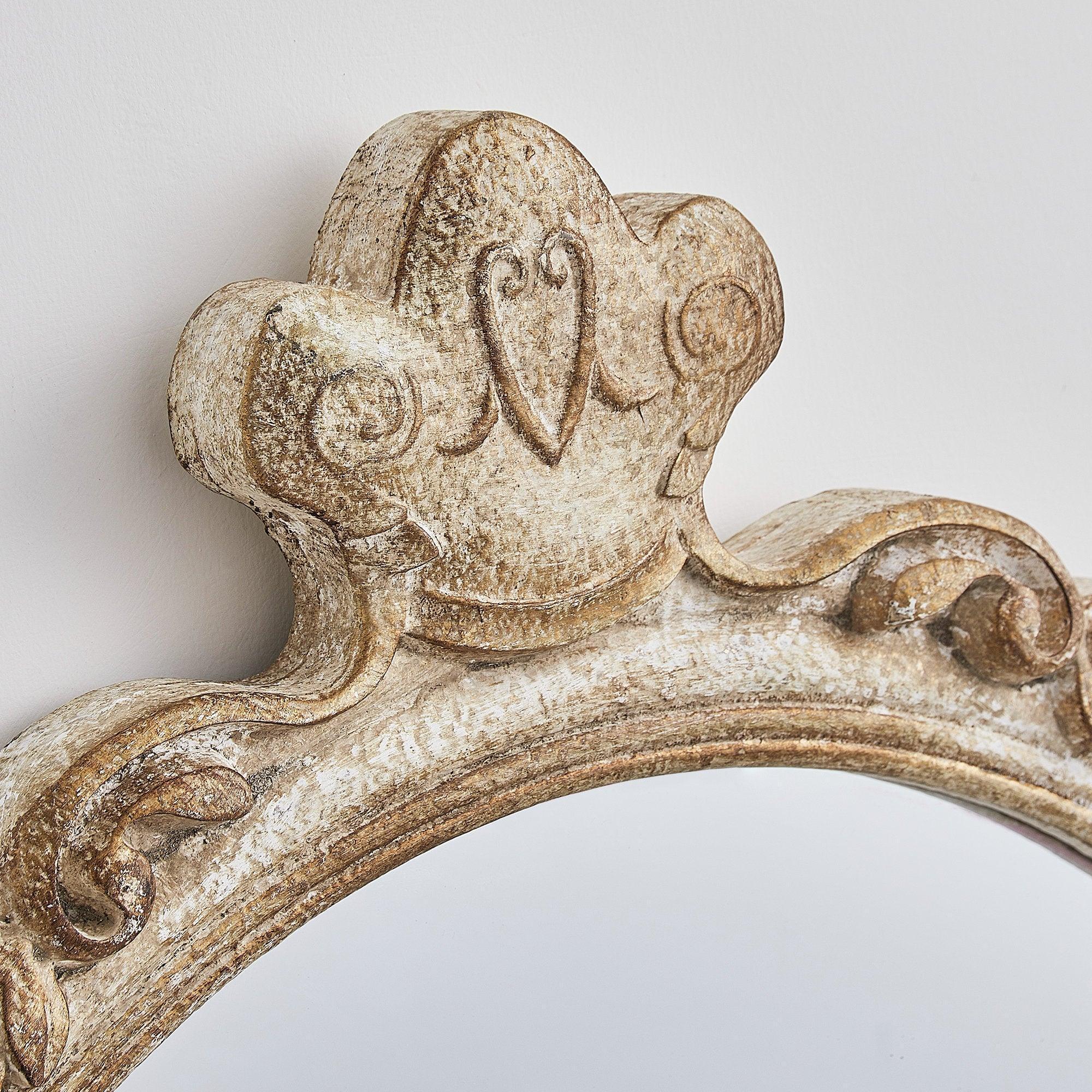 Close-up of carved crest detail on distressed wood oval mirror frame.