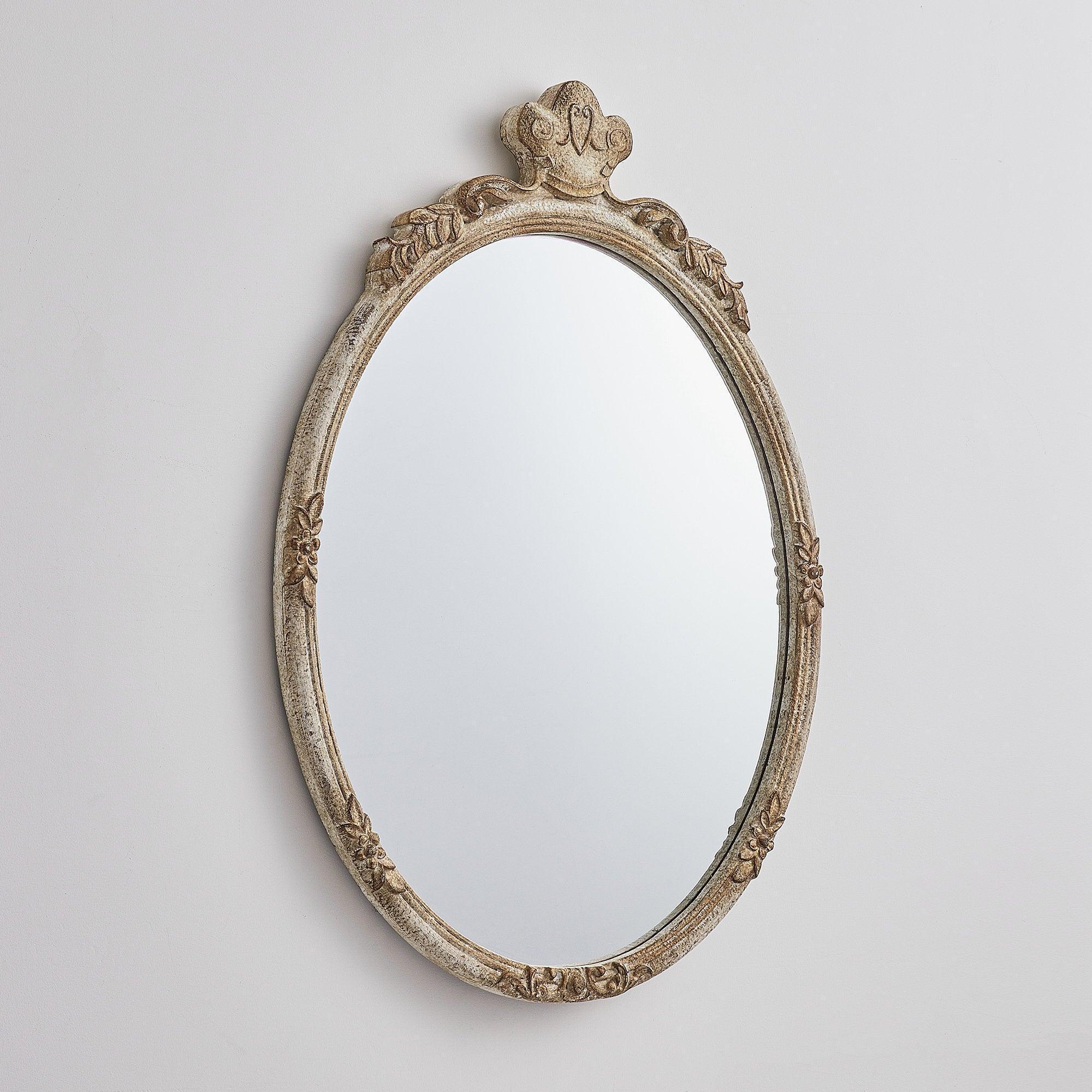 Oval wall mirror with distressed wood frame and decorative crown at the top.
