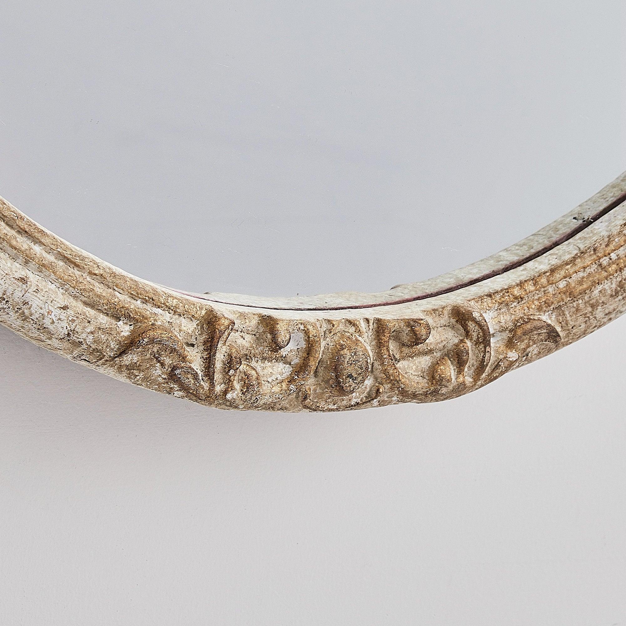 Close-up of ornate carved section on distressed wood oval mirror frame.