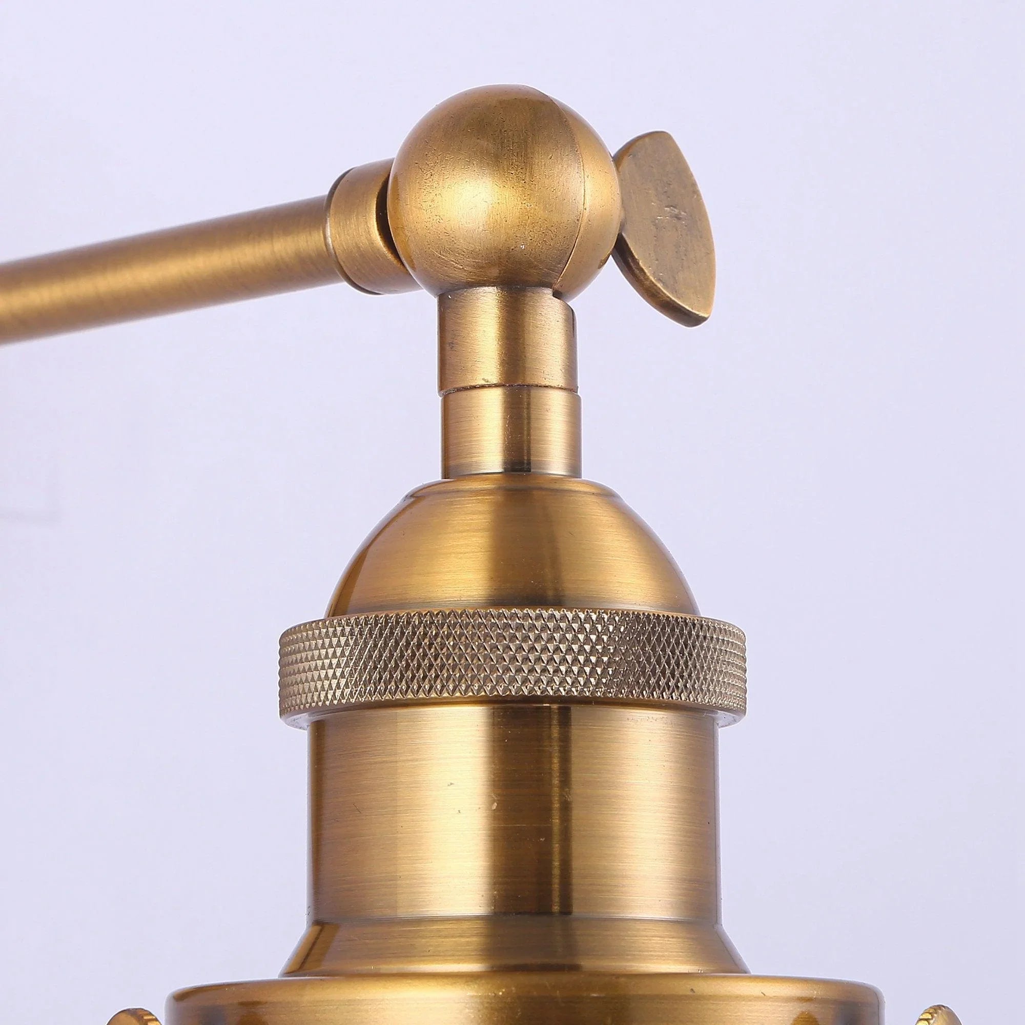Golden wall light detail: ball joint arm and textured collar above rattan shade