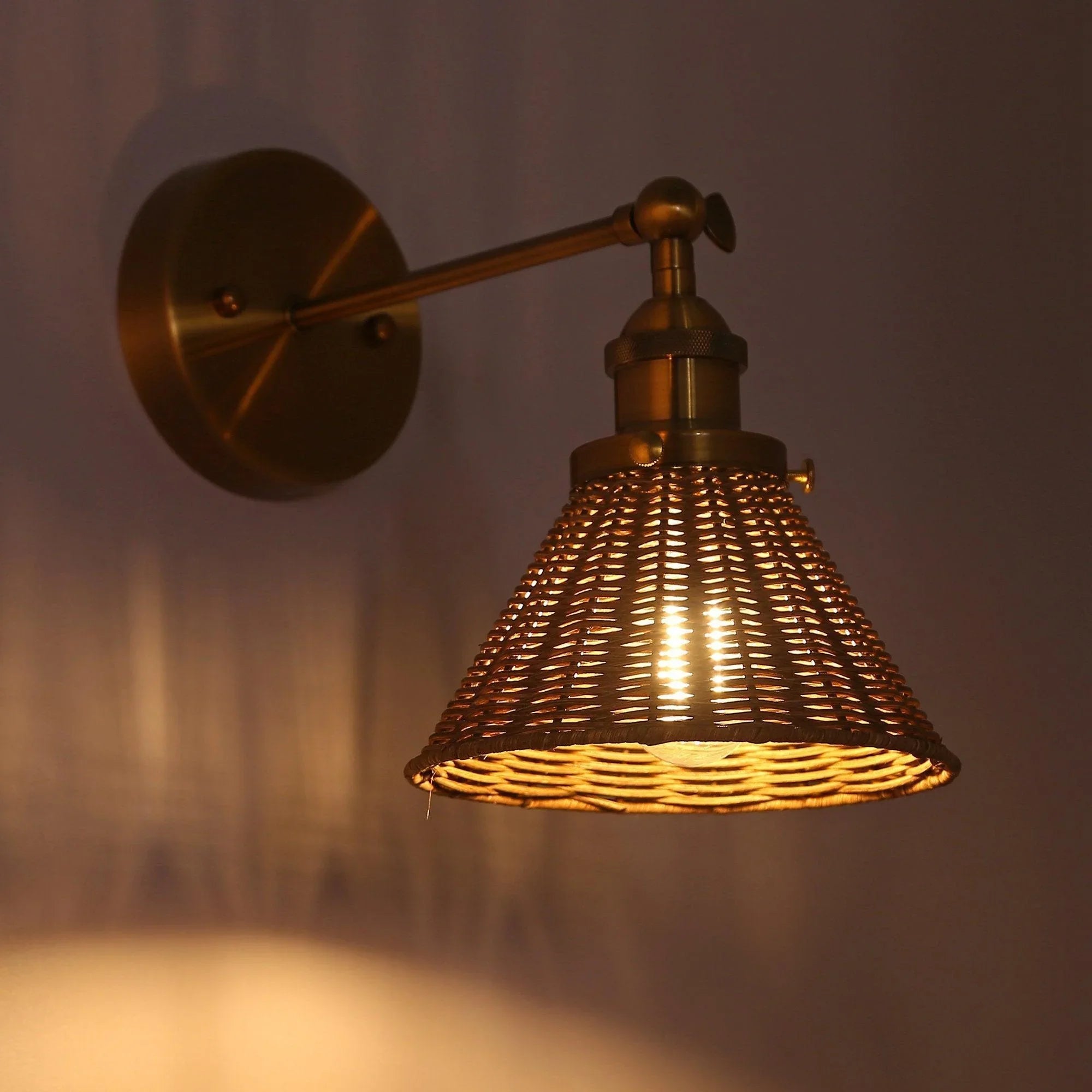 Golden wall sconce with woven rattan cone shade and lit glass bulb inside