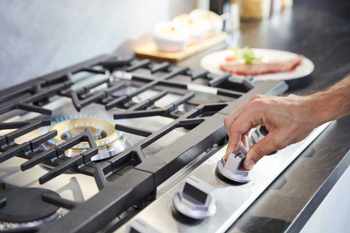 Hand adjusting front control knob on stainless steel gas cooktop with black grates