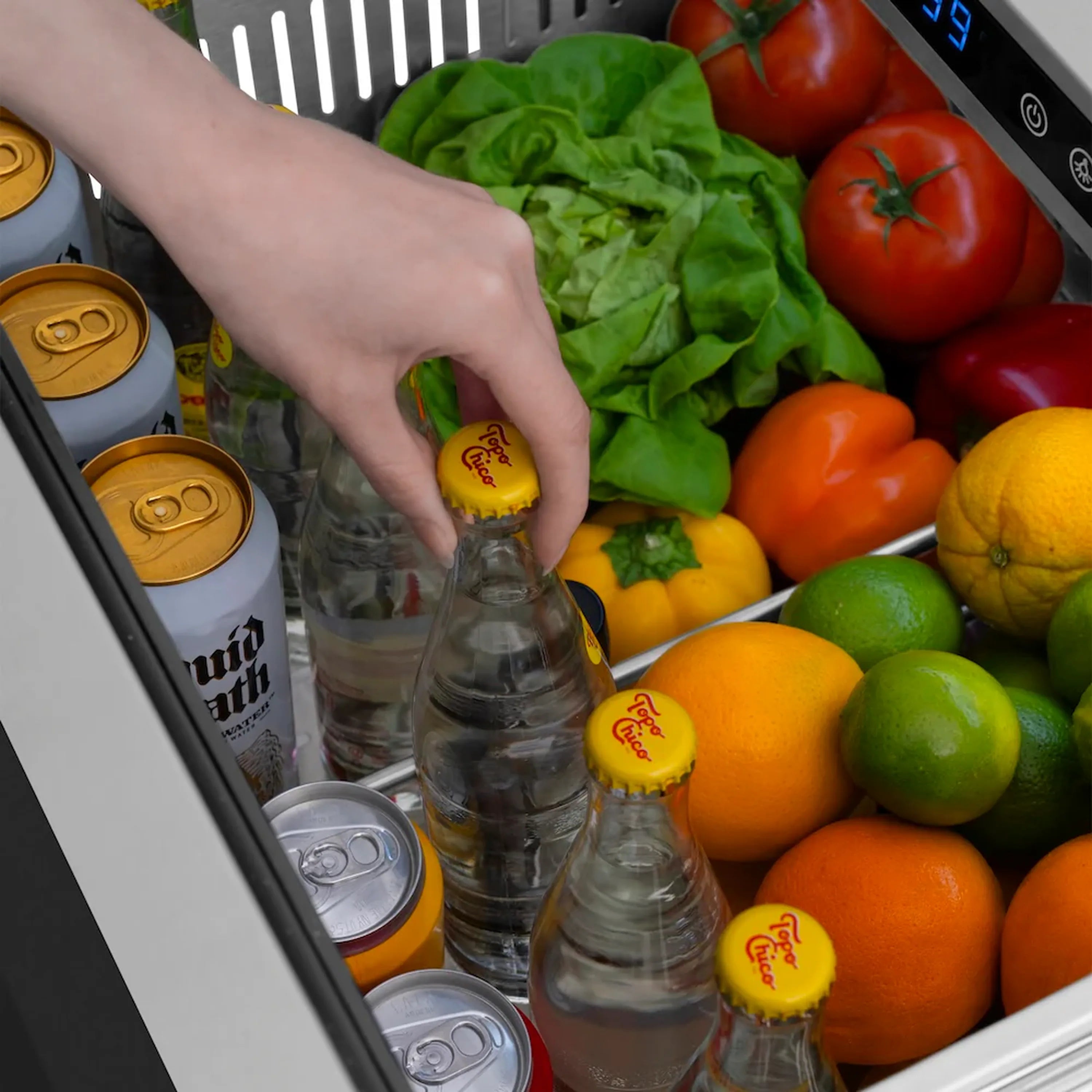 Stainless refrigerator drawer interior with hand placing capped bottle among produce