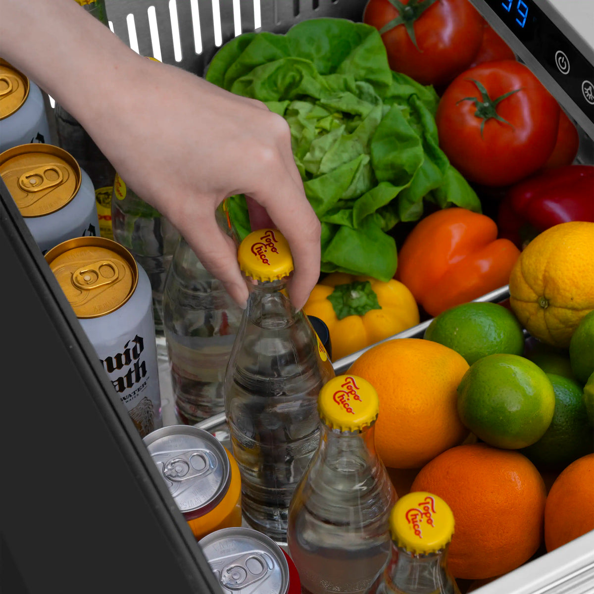 Refrigerator drawer interior with bottles and vegetables; hand holding a bottle