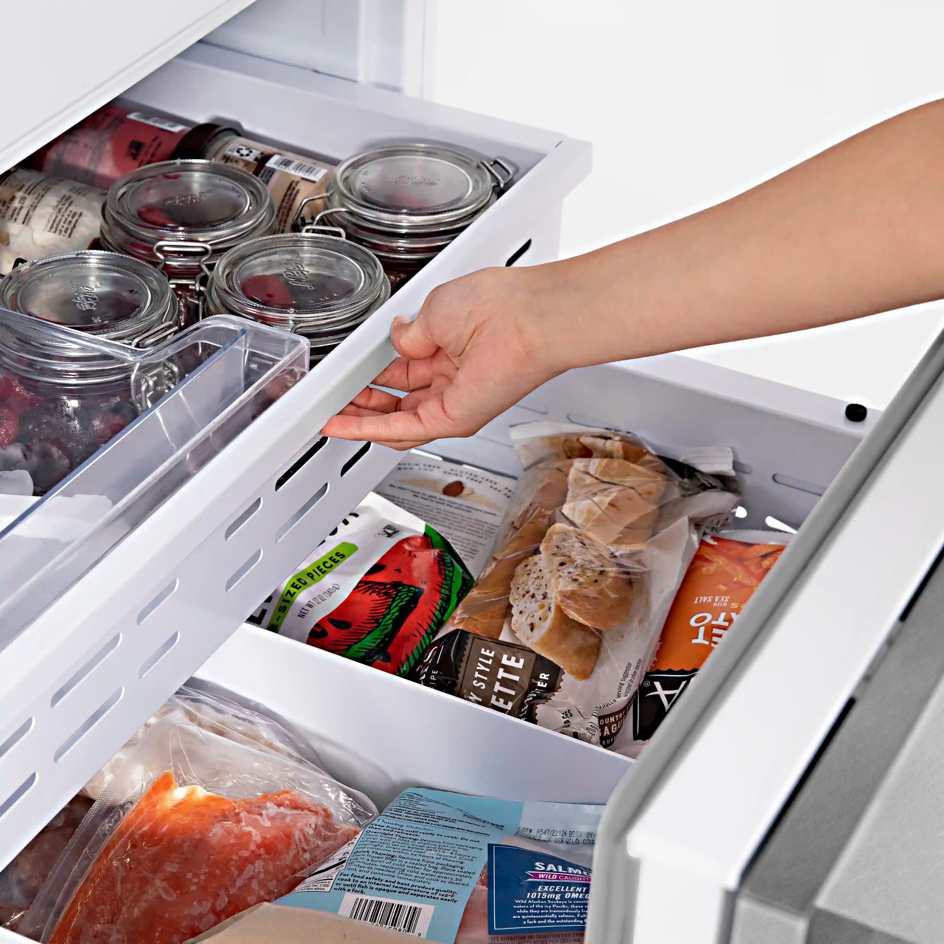 Bottom freezer drawer open with jars and packaged food on shelves